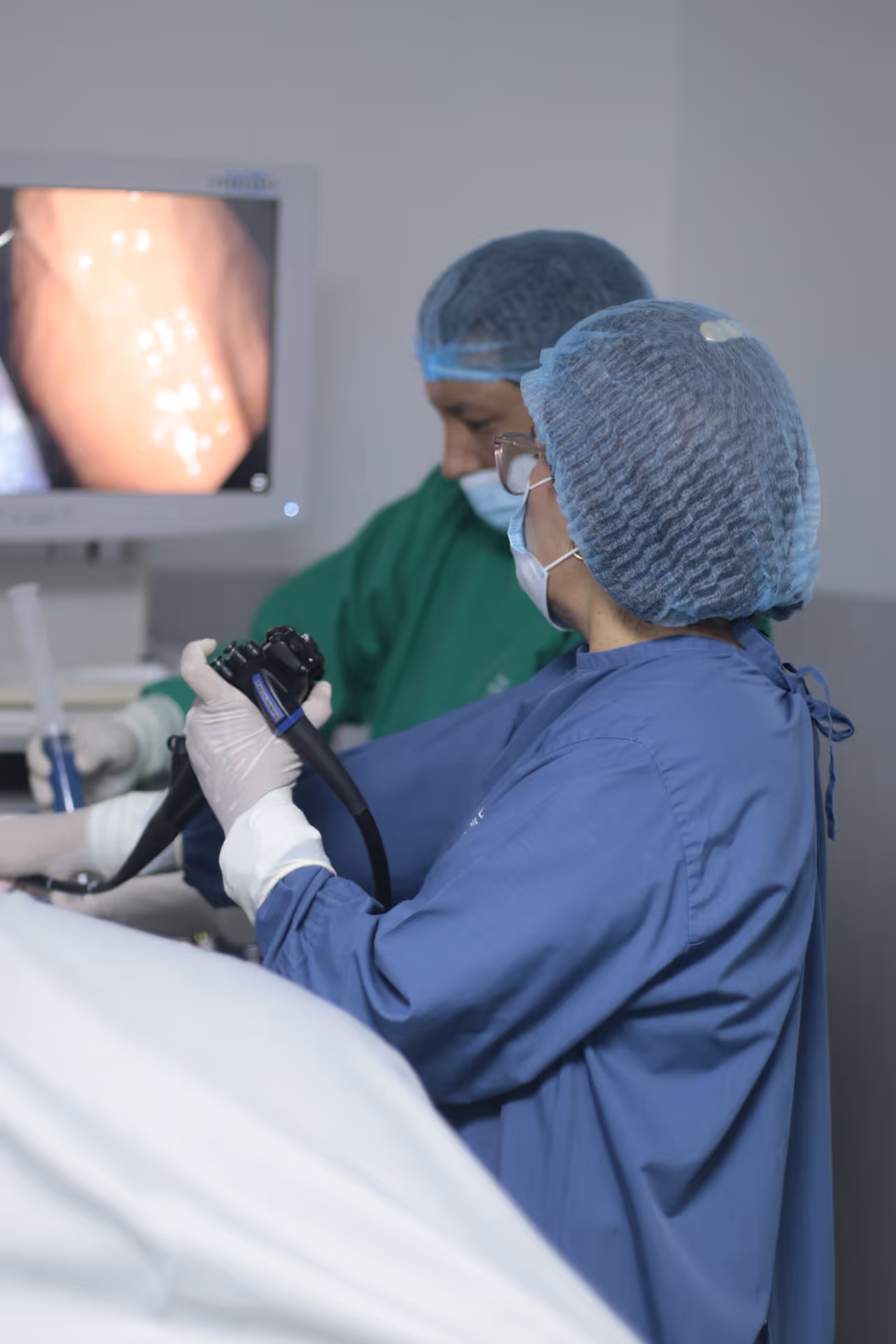 Manos con guantes lilas sosteniendo un endoscopio negro en un entorno médico.